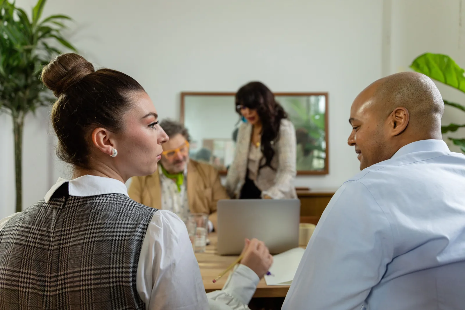 Four colleagues talking around a table in a bright office, one standing